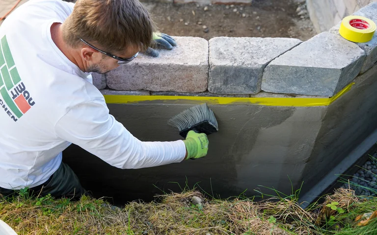 Die Außenwand der Gartenmauer wird mit Dichtschlämme flexibel abgedichtet.