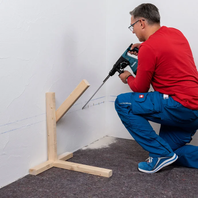 Handwerker bohrt mit einem Winkel von 45 Grad in die markierten Bohrl&ouml;cher der ersten Reihe.