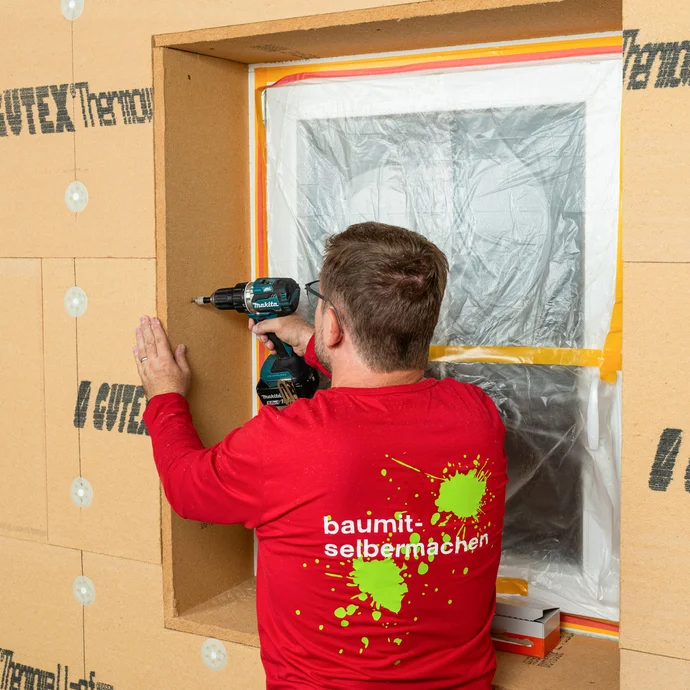 Baumit Heimwerker verschraubt die angeklebte Holzfaserdämmplatte in der seitlichen Laibung des Fensters. Innendämmung selber einbauen mit Holztragkonstruktion. Baumit Anleitung zum Selbermachen.