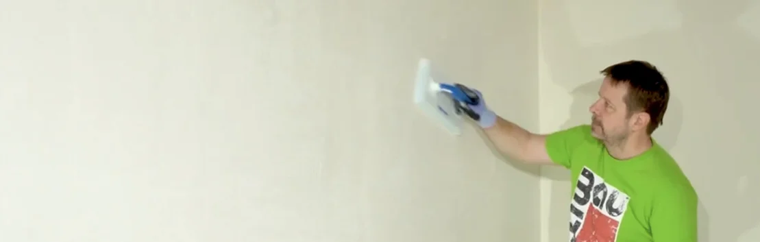 Mann gl&auml;ttet wei&szlig;e Wand mit Spachtelmasse, DIY-Tipps f&uuml;r glatte Oberfl&auml;chen.