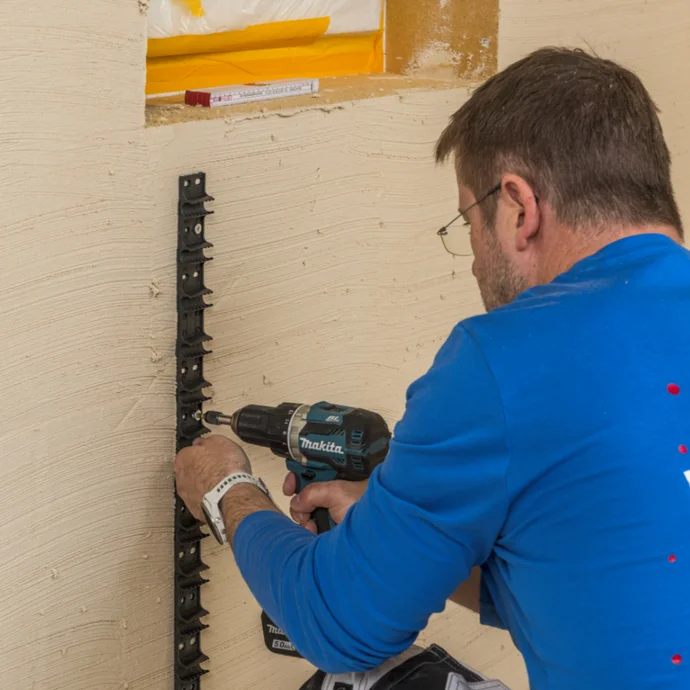 Heimwerker befestigt F&uuml;hrungsschienen f&uuml;r das Verputzen mit Bohrmaschine an einer Wand, Schritt f&uuml;r Schritt Anleitung.