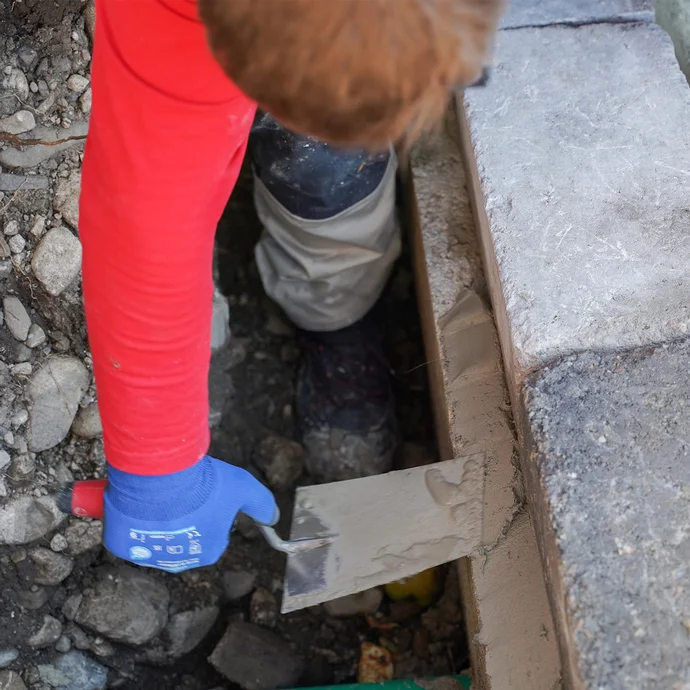 Eine Person zieht mit einer Kelle den Gefälle- und Betonspachtel entlang der Mauerkante auf, um die Hohlkehle zu erstellen.