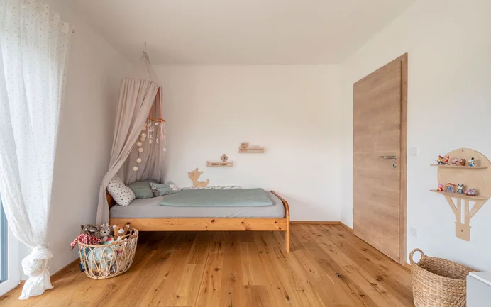 Moderne kinderkamer met een bed, speelgoed, een houten vloer en de stralend witte afwerkpleister InStyle Edelwit met een gevilte pleisterstructuur voor een aangenaam binnenklimaat.