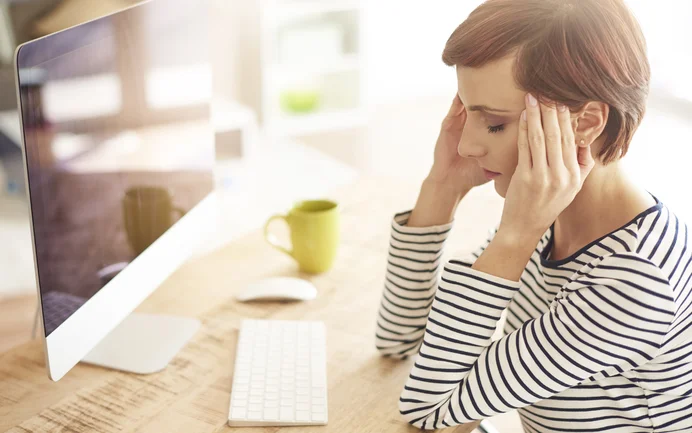 Schimmelsporen können Kopfschmerzen verursachen. Frau sitzt mit Kopfschmerzen am Schreibtisch vor dem Computer.