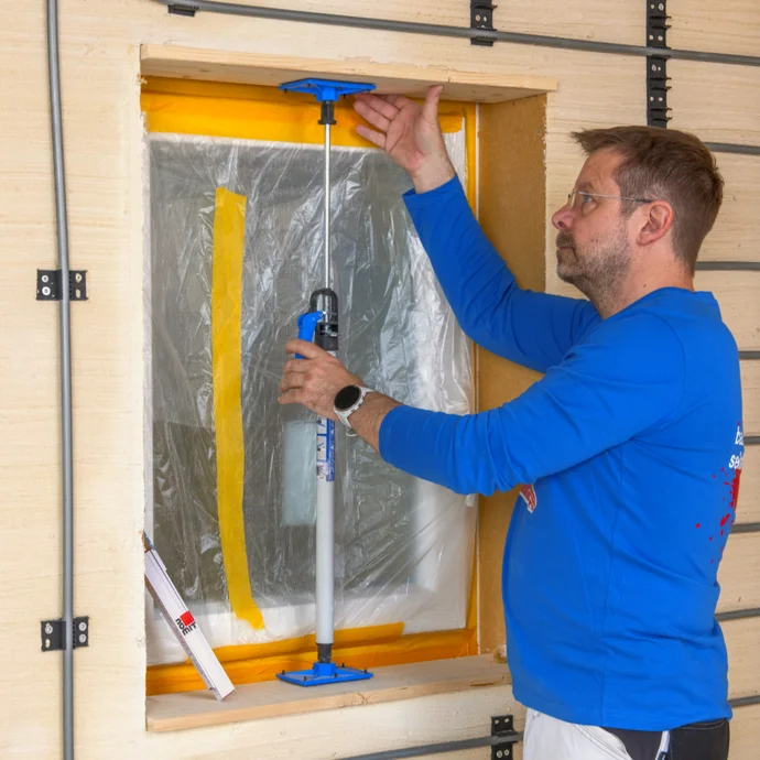Heimwerker richtet Fensterrahmen mit Montagekeil aus, um Isolierung anzubringen. Fassade mit D&auml;mmplatten verkleidet.