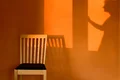 Holzstuhl vor orange gestrichener Wand mit Schattenspiel einer Person an einem Fenster im Hintergrund. Ideal für kreative Wandgestaltung.