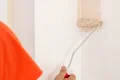 Person streicht Wand mit Farbroller; erste Schicht helles Beige, renovieren leicht gemacht.
