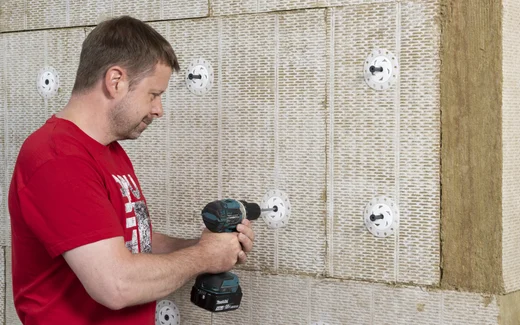 Heimwerker befestigt D&auml;mmplatten an der Wand mit Bohrmaschine und D&uuml;beln.