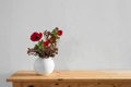 Holztisch mit Vase voller roter Blumen vor einer feinen, weißen Putzwand für einfachen Heimwerker-Stil.
