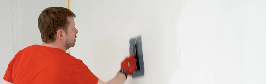 Mann verputzt eine Wand mit einer Gl&auml;ttkelle im Eigenbauprojekt.
