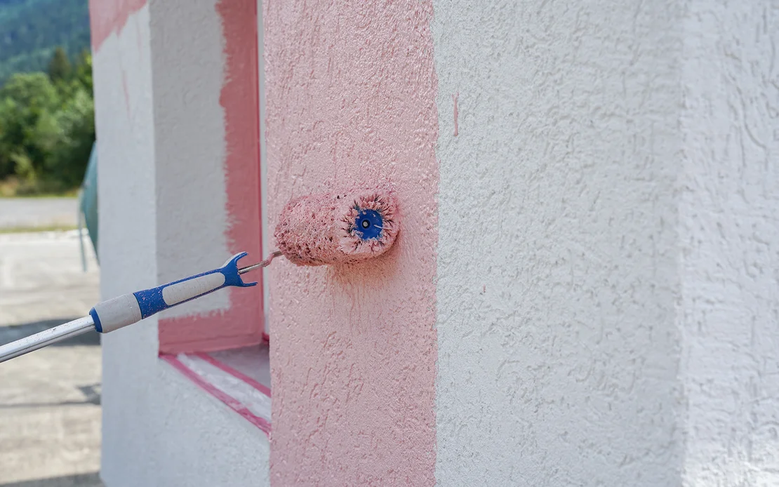 Eine wei&szlig;e Wand wird mit einer gro&szlig;en Farbrolle rosa gestrichen.
