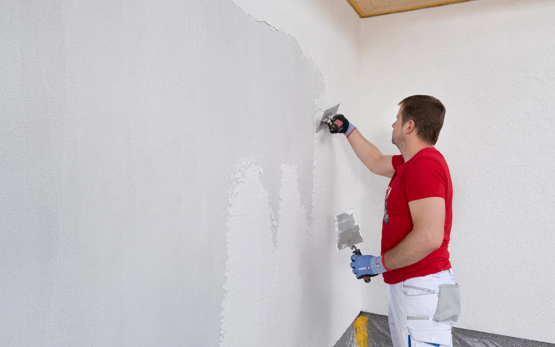 Heimwerker tr&auml;gt glatten Putz mit einer Kelle auf eine Innenwand auf.