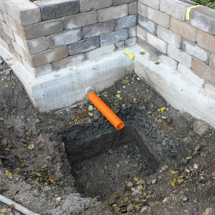 Gartenmauer mit ausgehobener Baugrube am Boden für die Sickerbox. Darüber ist das Drainagerohr erkennbar.