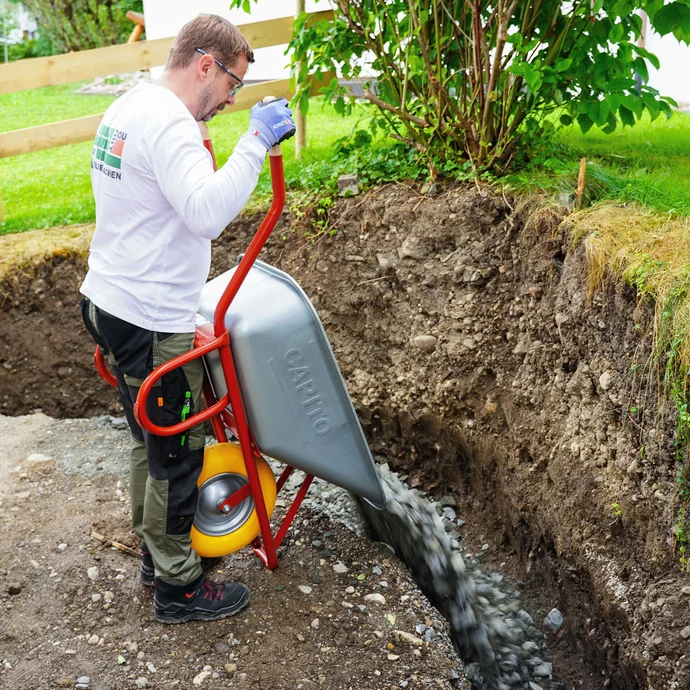 Bringe die Frostschutzschicht aus wasserdurchlässigem Schotter mit Hilfe einer Schubkarre in die Baugrube ein.