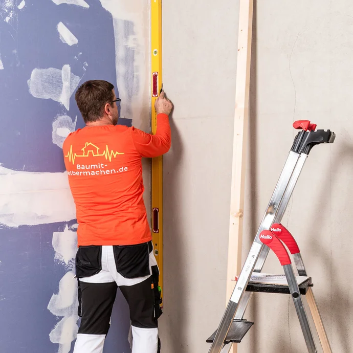 Heimwerker markiert die Position des ersten Kantholzes mit einer langen Wasserwaage und Stift an der Wand. Die Position ist sehr wichtig für den richtigen Aufbau der Tragkonstruktion für die Innendämmung.