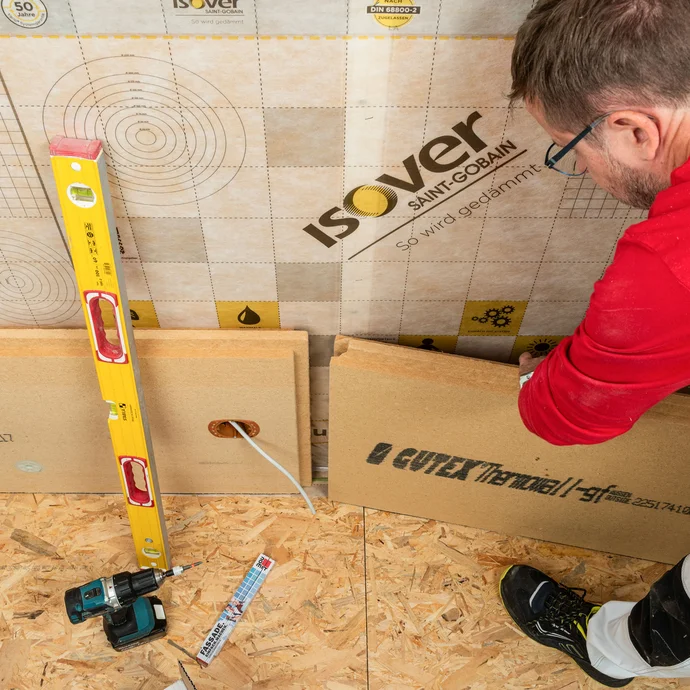 Heimwerker verbindet Holzfaserdämmplatten per Nut-und-Feder-Verbindung bei der Innendämmung. Die Wasserwaage zur Kontrolle liegt bereit.