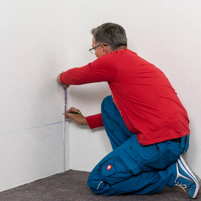 Handwerker zeichnet die zweite Bohrlochreihe 5 cm &uuml;ber der ersten Bohrlochreihe an.